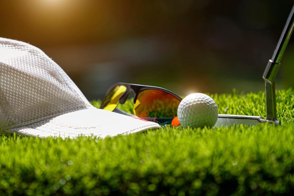 Golf Sonnenbrille mit Golfball und Cap auf dem Rasen im Sonnenlicht - Hero Tablet